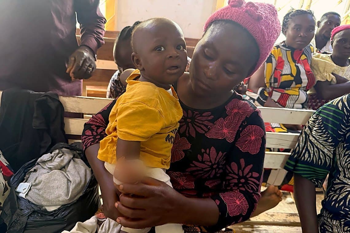 Gloria holding her baby daughter, whose hand is bandaged, among families gathered in Plateau State