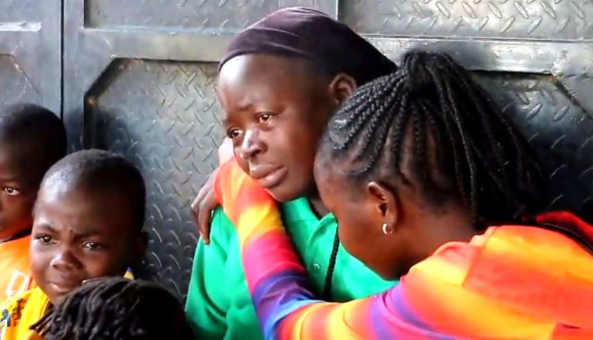 Ladidi Sunday in tears, embraced by a woman, with her children beside her